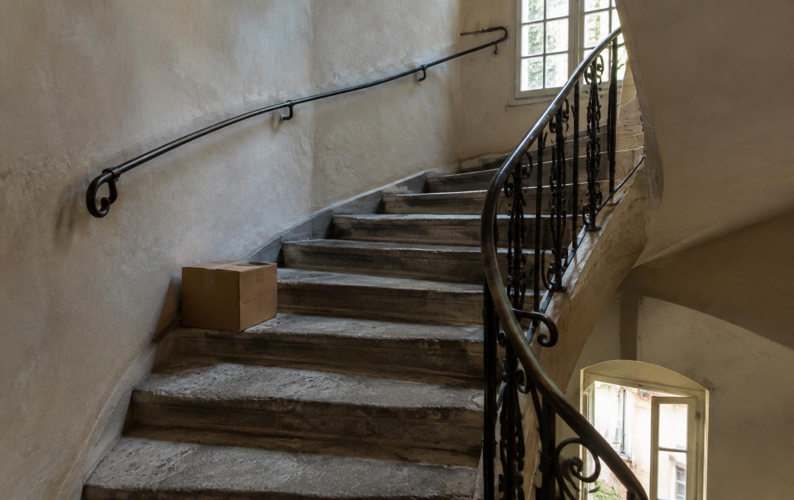 Escalier en pierre étroit d'un immeuble ancien, avec un carton sur une marche